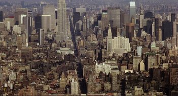 Movie still from “Koyaanisqatsi” (1982), directed by Godfrey Reggio – An aerial view of a large city with skyscrapers; Extreme Wide shot, High angle