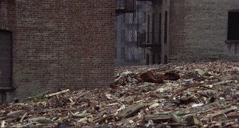 Movie still from “Koyaanisqatsi” (1982), directed by Godfrey Reggio – A pile of debris in front of a brick building; Extreme Wide shot, High angle