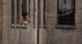 Movie still from “Koyaanisqatsi” (1982), directed by Godfrey Reggio – A woman eating a donut from a window sill; Extreme Wide shot, High angle