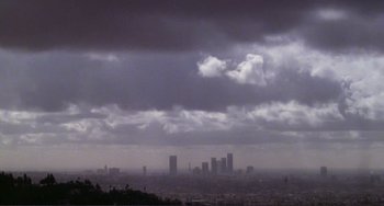 Movie still from “Koyaanisqatsi” (1982), directed by Godfrey Reggio – A view of a city skyline under a cloudy sky; Extreme Wide shot, High angle