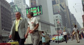 Movie still from “Koyaanisqatsi” (1982), directed by Godfrey Reggio – A man walking down a street next to a van; Wide shot, Low angle
