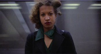 Movie still from “Koyaanisqatsi” (1982), directed by Godfrey Reggio – A woman with curly hair wearing a green neck tie; Close Up shot, Low angle
