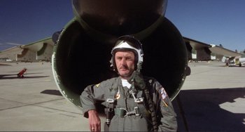 Movie still from “Koyaanisqatsi” (1982), directed by Godfrey Reggio – A man in a flight suit standing in front of an airplane; Medium shot, Low angle