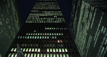 Movie still from “Koyaanisqatsi” (1982), directed by Godfrey Reggio – A tall building lit up at night with green lights; Extreme Wide shot, Low angle