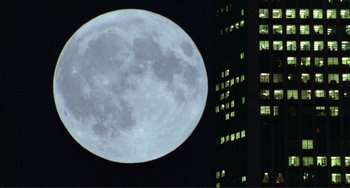 Movie still from “Koyaanisqatsi” (1982), directed by Godfrey Reggio – A full moon in the night sky over a building; Extreme Wide shot, Low angle