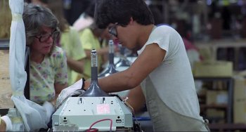 Movie still from “Koyaanisqatsi” (1982), directed by Godfrey Reggio – A man working on a machine in an assembly shop; Medium shot, Low angle