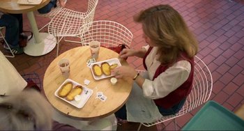 Movie still from “Koyaanisqatsi” (1982), directed by Godfrey Reggio – A woman sitting at a table with food on it; Wide shot, High angle