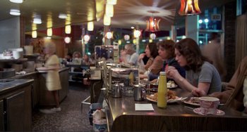 Movie still from “Koyaanisqatsi” (1982), directed by Godfrey Reggio – People are sitting at a table in a restaurant; Wide shot, Over the shoulder angle