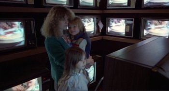 Movie still from “Koyaanisqatsi” (1982), directed by Godfrey Reggio – A woman and two children looking at a television screen; Medium shot, Over the shoulder angle