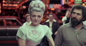 Movie still from “Koyaanisqatsi” (1982), directed by Godfrey Reggio – An older woman with a very large hair style; Medium shot, High angle