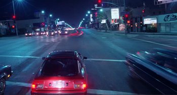 Movie still from “Koyaanisqatsi” (1982), directed by Godfrey Reggio – A red car driving down a street at night; Extreme Wide shot, High angle
