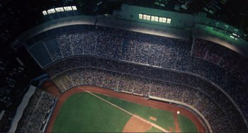 Movie still from “Koyaanisqatsi” (1982), directed by Godfrey Reggio – An aerial view of a baseball field with a lot of fans; Extreme Wide shot, Overhead angle