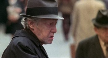 Movie still from “Koyaanisqatsi” (1982), directed by Godfrey Reggio – An older man wearing a hat and a black shirt; Close Up shot, Over the shoulder angle