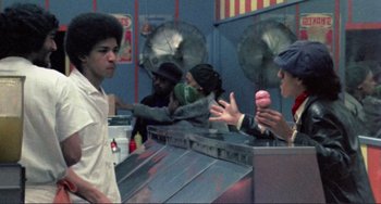 Movie still from “Koyaanisqatsi” (1982), directed by Godfrey Reggio – A group of young men standing around a donut shop; Medium shot, Over the shoulder angle