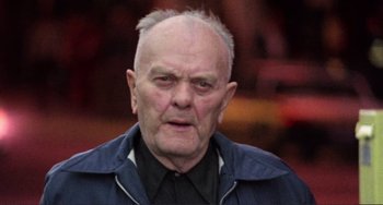 Movie still from “Koyaanisqatsi” (1982), directed by Godfrey Reggio – An old man with a shaved head is looking at the camera; Close Up shot, Low angle