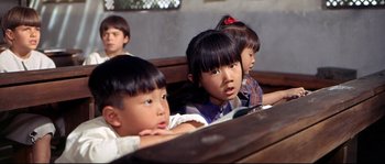 Movie still from “Krakatoa: East of Java” (1968), directed by Bernard L. Kowalski – A group of children sitting in a row on a bench; Close Up shot, High angle
