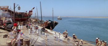 Movie still from “Krakatoa: East of Java” (1968), directed by Bernard L. Kowalski – A group of people walking along a pier; Extreme Wide shot, High angle