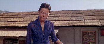 Movie still from “Krakatoa: East of Java” (1968), directed by Bernard L. Kowalski – A woman in a blue shirt standing in front of a building; Medium shot, Low angle