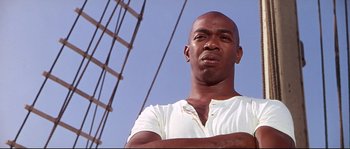 Movie still from “Krakatoa: East of Java” (1968), directed by Bernard L. Kowalski – A man with his arms crossed standing on a boat; Close Up shot, Low angle
