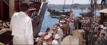 Movie still from “Krakatoa: East of Java” (1968), directed by Bernard L. Kowalski – A group of people standing on a dock next to a boat; Wide shot, High angle