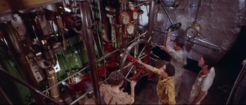 Movie still from “Krakatoa: East of Java” (1968), directed by Bernard L. Kowalski – Two men working on a machine in an industrial setting; Medium shot, High angle