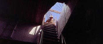 Movie still from “Krakatoa: East of Java” (1968), directed by Bernard L. Kowalski – A man wearing a hat is standing on some stairs; Wide shot, Low angle