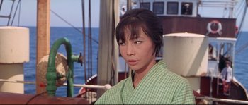 Movie still from “Krakatoa: East of Java” (1968), directed by Bernard L. Kowalski – A woman in a green checkered robe sitting in front of a boat; Close Up shot, Over the shoulder angle