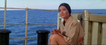 Movie still from “Krakatoa: East of Java” (1968), directed by Bernard L. Kowalski – A woman sitting on a dock near the ocean; Medium shot, High angle