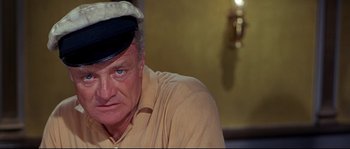 Movie still from “Krakatoa: East of Java” (1968), directed by Bernard L. Kowalski – An older man wearing a sailor's hat and a yellow shirt; Close Up shot, High angle