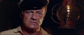 Movie still from “Krakatoa: East of Java” (1968), directed by Bernard L. Kowalski – An older man wearing a black hat and a tan shirt; Close Up shot, Low angle