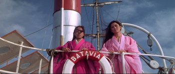 Movie still from “Krakatoa: East of Java” (1968), directed by Bernard L. Kowalski – Two women in pink robes standing next to a boat; Medium shot, Low angle