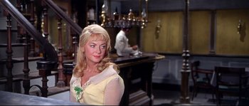 Movie still from “Krakatoa: East of Java” (1968), directed by Bernard L. Kowalski – A woman in a yellow dress sitting in front of a bar; Medium shot, Over the shoulder angle