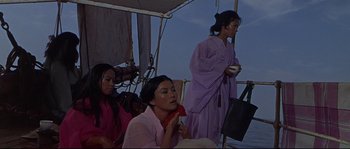 Movie still from “Krakatoa: East of Java” (1968), directed by Bernard L. Kowalski – A group of women sitting on top of a boat in the water; Medium shot, High angle