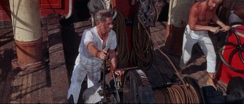 Movie still from “Krakatoa: East of Java” (1968), directed by Bernard L. Kowalski – An old man working on a boat on the water; Medium shot, High angle