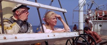 Movie still from “Krakatoa: East of Java” (1968), directed by Bernard L. Kowalski – A woman sitting in a boat on the beach; Medium shot, Over the shoulder angle