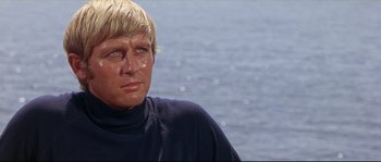 Movie still from “Krakatoa: East of Java” (1968), directed by Bernard L. Kowalski – A person wearing a wetsuit near a body of water; Close Up shot, Low angle