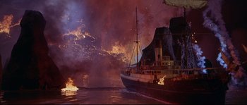 Movie still from “Krakatoa: East of Java” (1968), directed by Bernard L. Kowalski – A boat in the water near a large fire; Extreme Wide shot, High angle