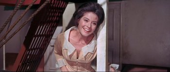 Movie still from “Krakatoa: East of Java” (1968), directed by Bernard L. Kowalski – A smiling woman leaning against a white wall; Close Up shot, Low angle