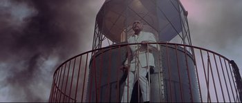Movie still from “Krakatoa: East of Java” (1968), directed by Bernard L. Kowalski – A man in a white suit standing in a metal tower; Wide shot, Low angle