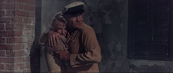 Movie still from “Krakatoa: East of Java” (1968), directed by Bernard L. Kowalski – An older man and woman hugging in a dark room; Medium shot, Low angle