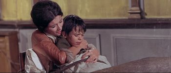 Movie still from “Krakatoa: East of Java” (1968), directed by Bernard L. Kowalski – A woman holding a young boy while he is holding a rope; Medium shot, High angle