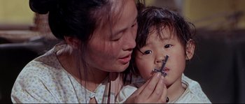 Movie still from “Krakatoa: East of Java” (1968), directed by Bernard L. Kowalski – An asian woman holding a small child with a razor; Close Up shot, High angle