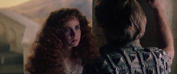 A woman with long red curly hair looking at a man with blue eyes