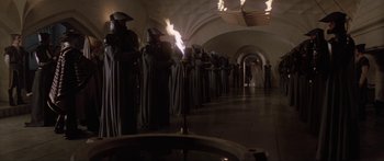 Movie still from “Krull” (1983), directed by Peter Yates – A group of people dressed in black and holding torches in a hallway; Wide shot, High angle