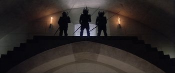Movie still from “Krull” (1983), directed by Peter Yates – A group of three people standing on top of a building; Wide shot, Low angle