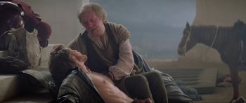 Movie still from “Krull” (1983), directed by Peter Yates – An old man sitting next to a shirtless man; Medium shot, Over the shoulder angle