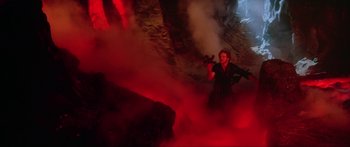 Movie still from “Krull” (1983), directed by Peter Yates – A woman holding a gun in a cave filled with red smoke; Wide shot, High angle