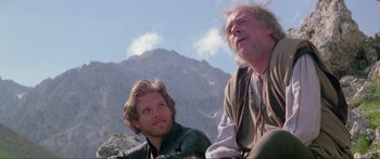 Movie still from “Krull” (1983), directed by Peter Yates – Two men sitting next to each other in front of a mountain range; Medium shot, Low angle