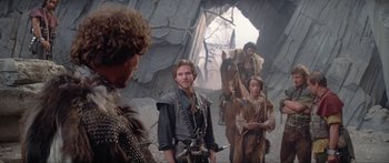 Movie still from “Krull” (1983), directed by Peter Yates – A group of men in medieval garb standing in front of a cave; Medium shot, Over the shoulder angle
