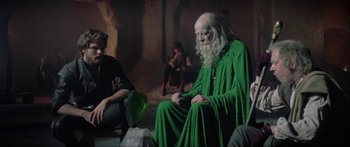 Movie still from “Krull” (1983), directed by Peter Yates – An old man dressed in green sitting on a chair; Medium shot, Over the shoulder angle